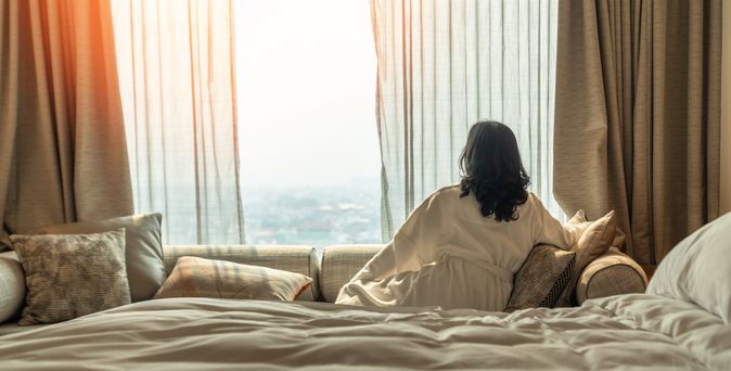Frau sitzt in Ihrem Hotelzimmer auf dem Sofa und schaut aus dem Fenster