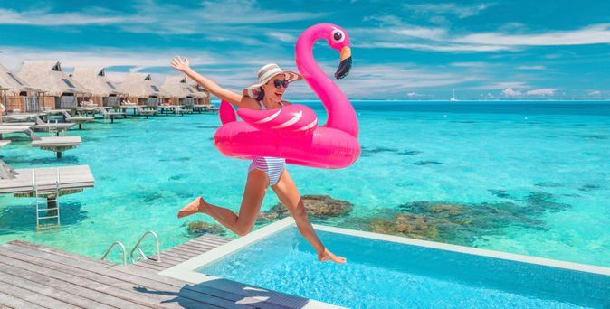 Eine Frau springt lachend mit einem Flamingo Schwimmreifen in einen Pool 
