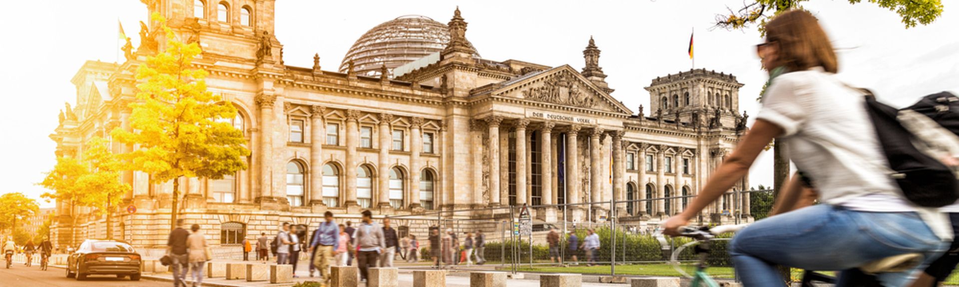 Eine Frau fährt bei Sonnenschein auf dem Fahrrad am Berliner Bundestag vorbei