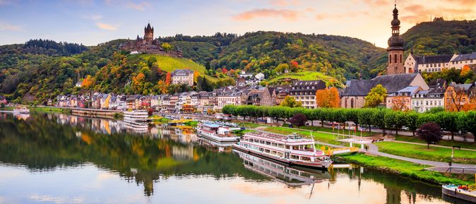 Schiffe am Ufer der Mosel mit Häusern und Sonnenuntergang im Hintergrund