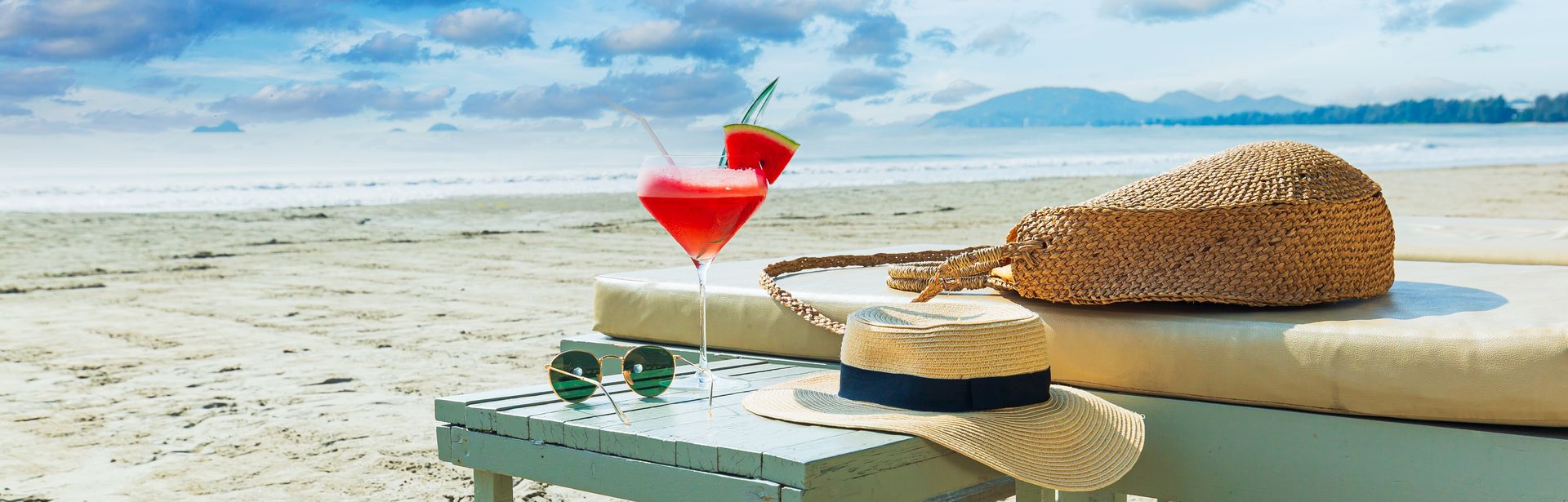 Strandliege mit Cocktail-Glas, Sonnernhut und Sonnebrille mit Blick auf den Strand und das Meer