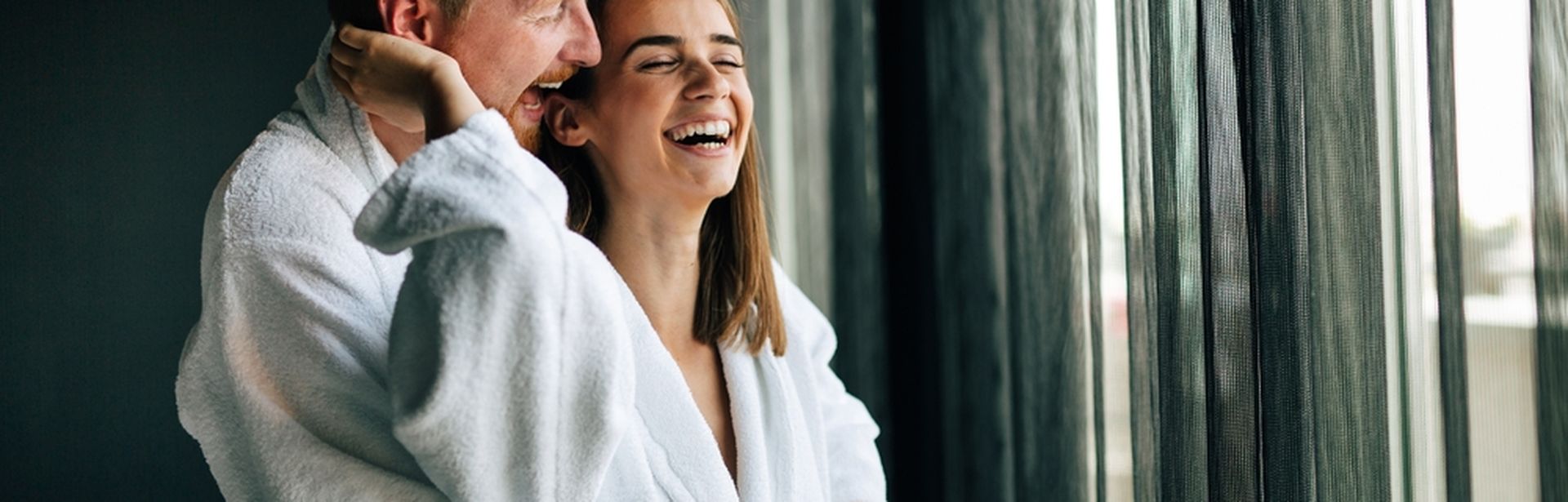 Ein Paar steht lachend vor einem Fenster