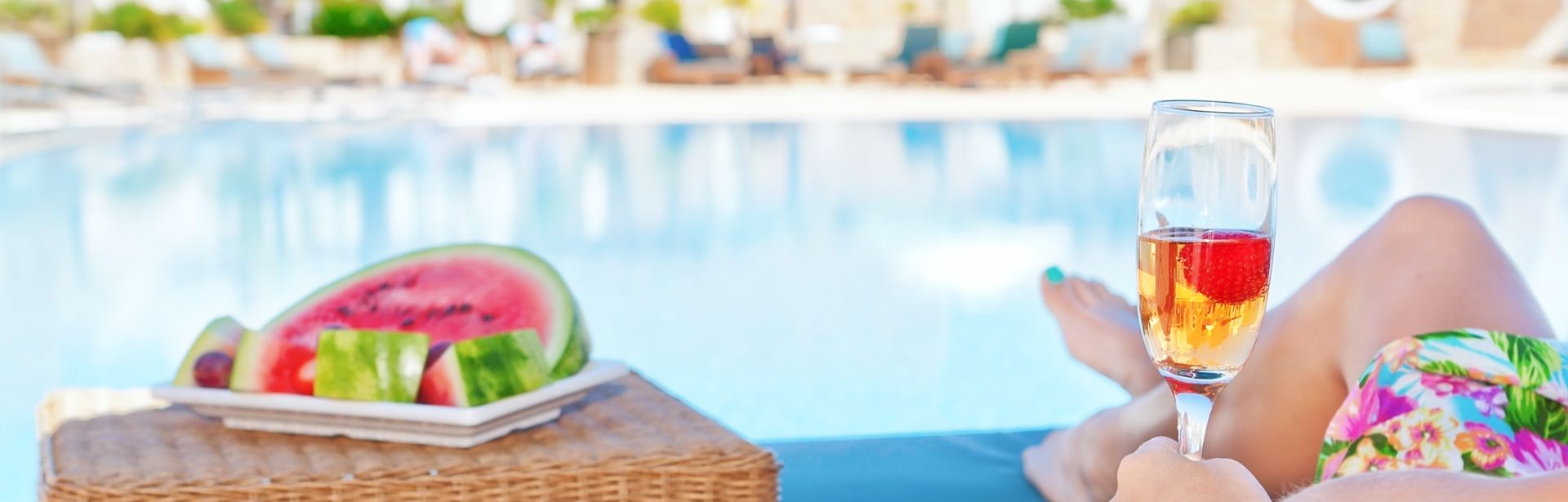 Person liegt am Pool mit Obst und Getränk