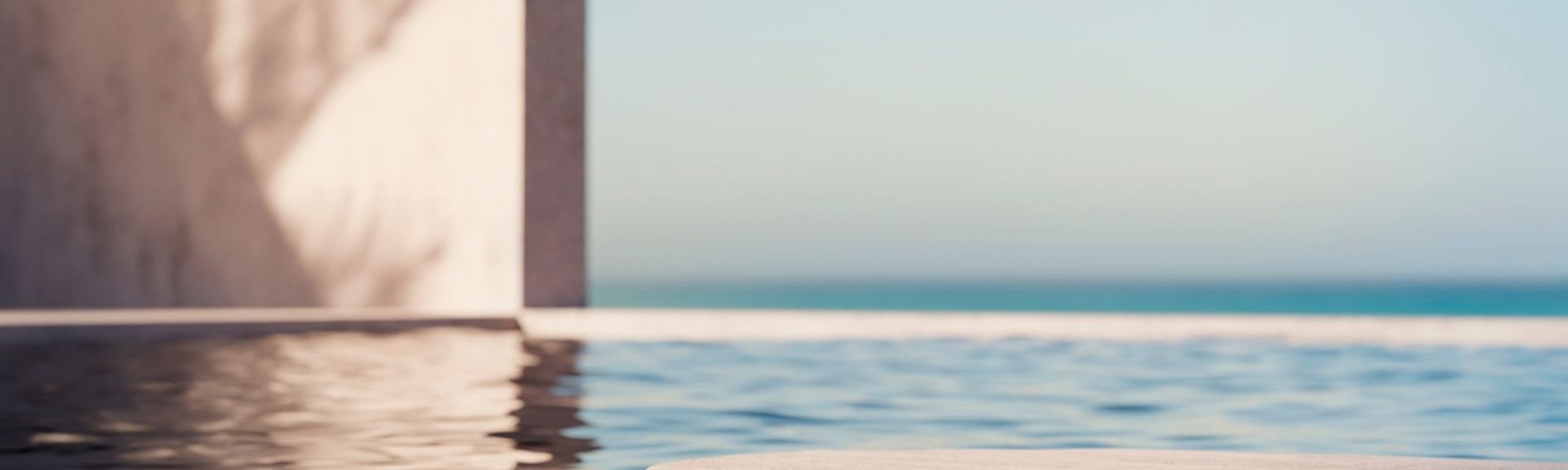 Eine Pooloberfläche auf der sich die Wand daneben spiegelt, im Hintergrund blauer Himmel