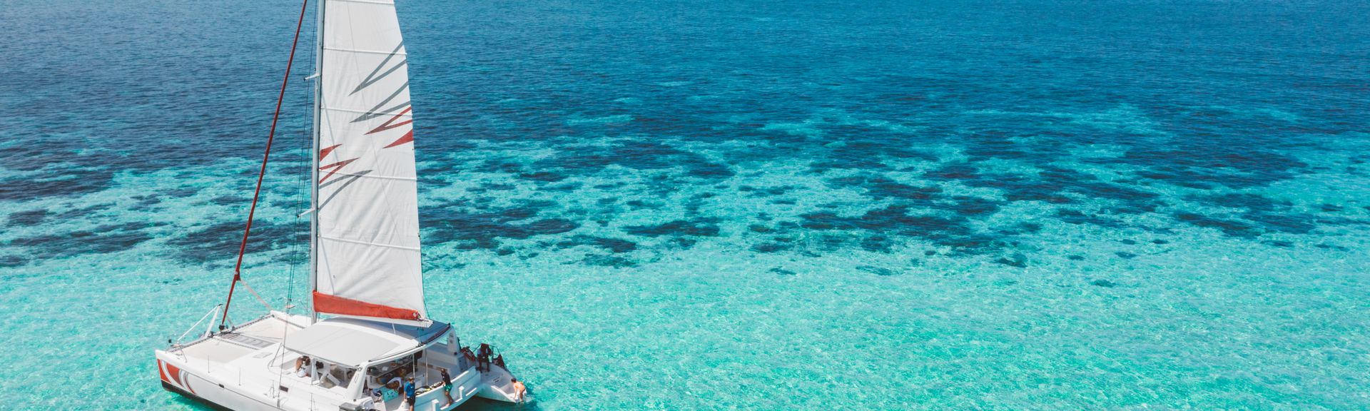 Ein Segelboot im Meer, dahinter schwimmen mehrere Personen