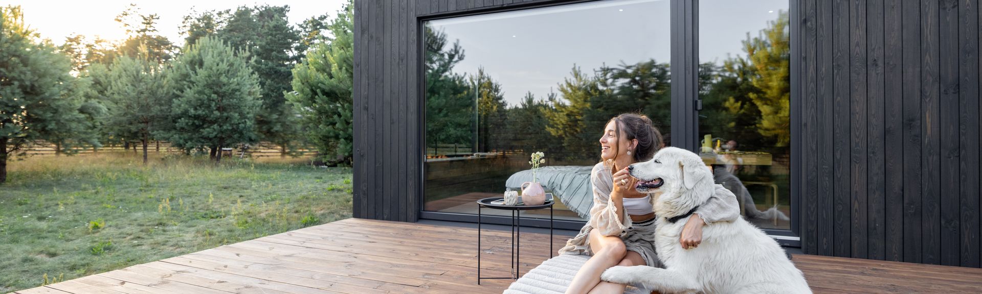 Eine Frau sitzt mit Ihrem Hund auf der Terasse von einem Ferienhaus
