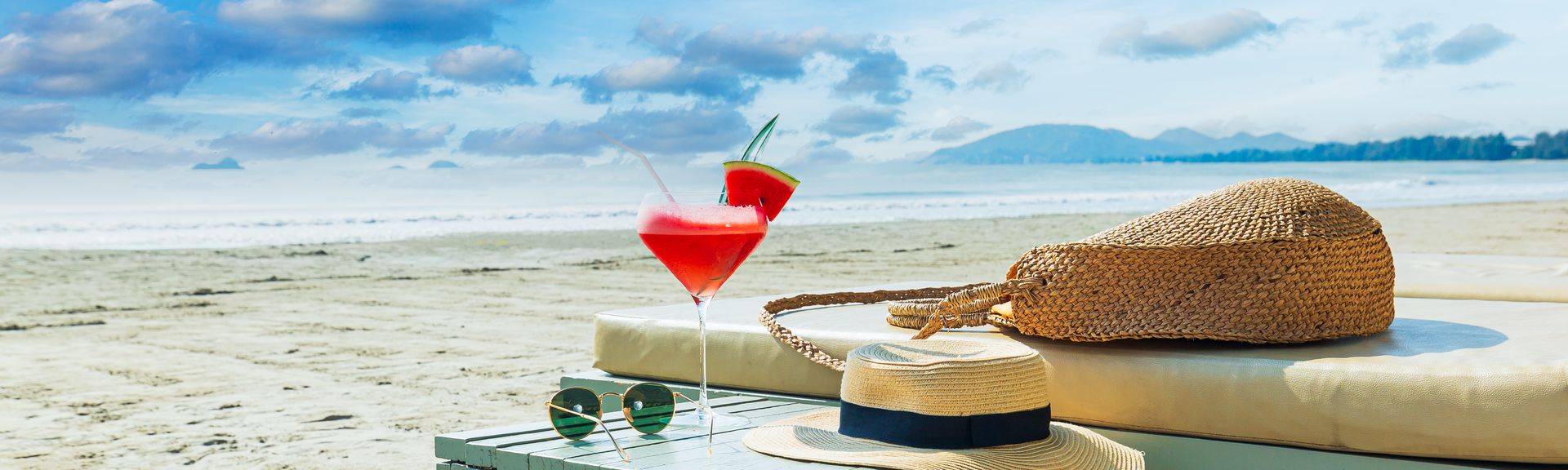 Eine Liege und ein Tisch mit einem Sonnenhut und einem Getränk am Strand