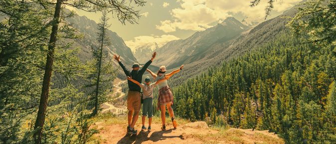 Eltern und Kind schauen beim Wandern gemeinsam auf eine Berglandschaft 