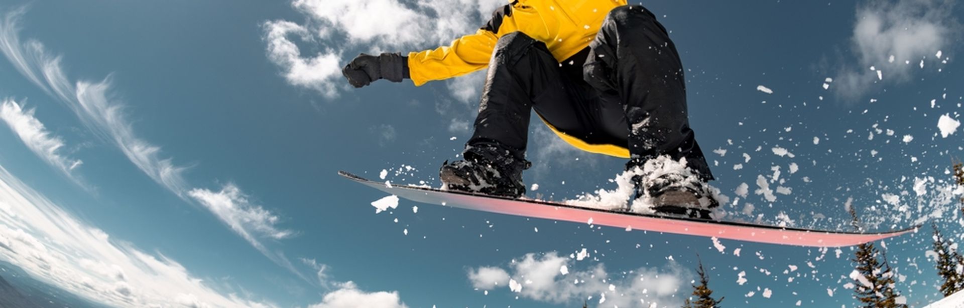 Eine Person in gelber Winterjacke springt mit einem Snowboard durch die Luft