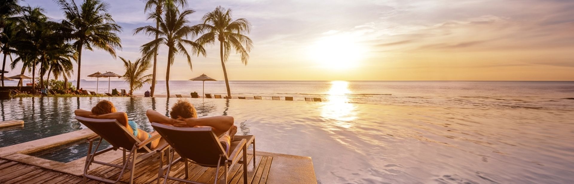 Zwei Personen liegen auf Liegen am Pool und schauen sich den Sonnenuntergang an