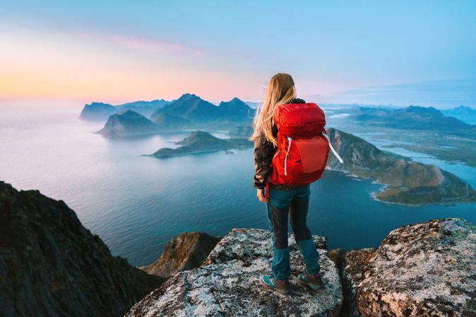 Alleinreisende Frau mit Rucksack schaut von einem Berg auf Wasser 
