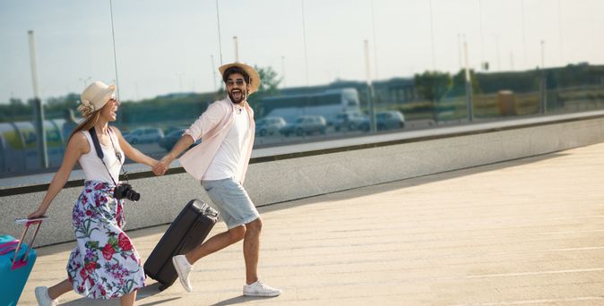 Ein Paar läuft mit Koffern aufgeregt einen Weg entlang