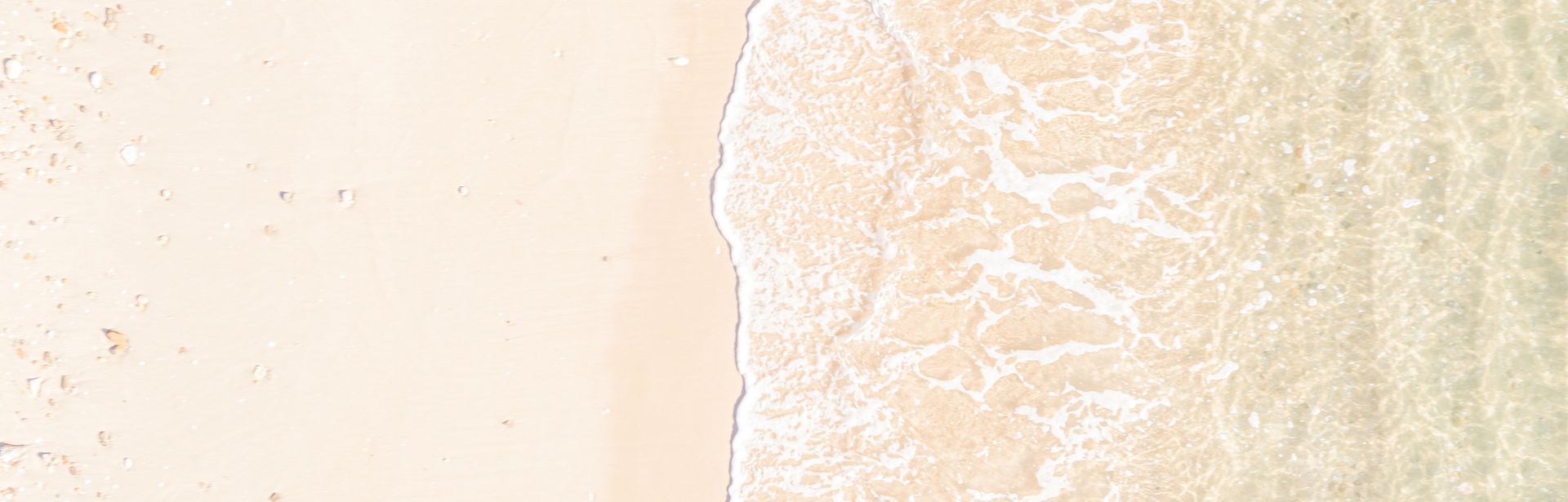 Eine Welle glasklares Wasser trifft auf einen weißen Sandstrand