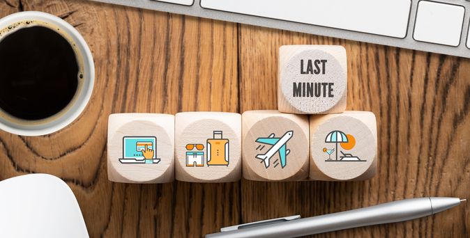 Auf einem Schreibtisch liegen Holzwürfel mit Symbolen drauf in einer Reihe und einem darüberliegenden Würfel, wo "Last Minute" drauf steht