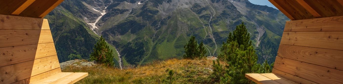 Aus einer Holzhütte mit zwei Bänken schaut man auf eine beeindruckende Berglandschaft