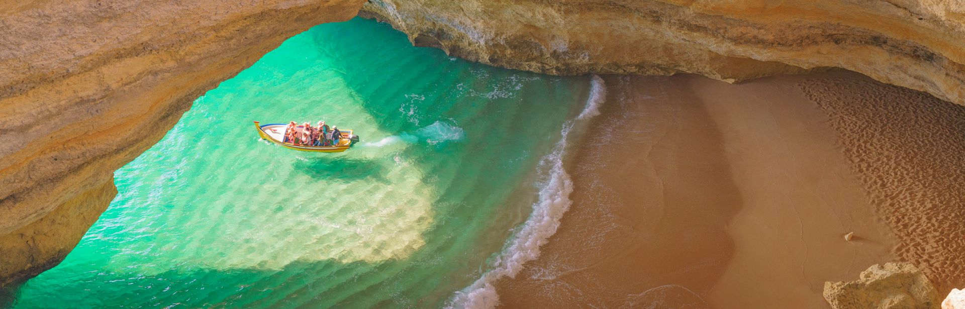 Ein kleines Boot mit Menschen an einer Küste auf dem Wasser unter einem Felsenbogen