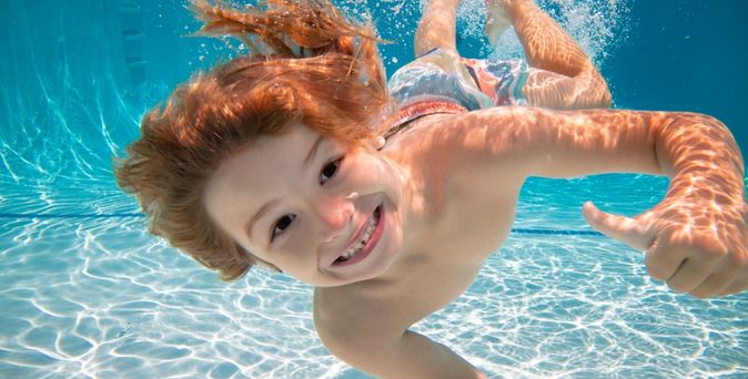 Lächelnder Junge taucht unter Wasser und zeigt beide Daumen nach oben