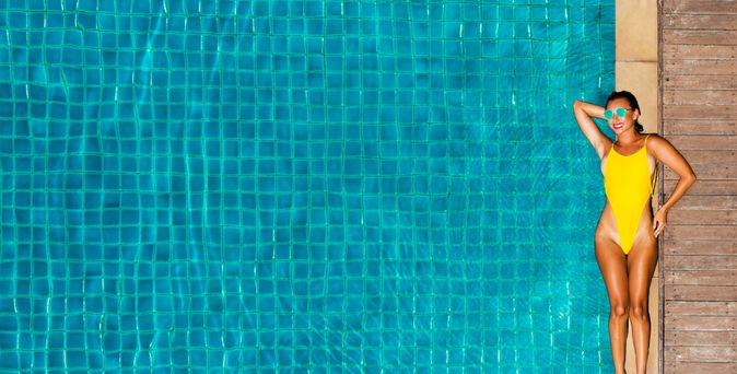 Ein großer Pool, am Rand liegt eine Frau im gelben Badeanzug und einer Sonnenbrille