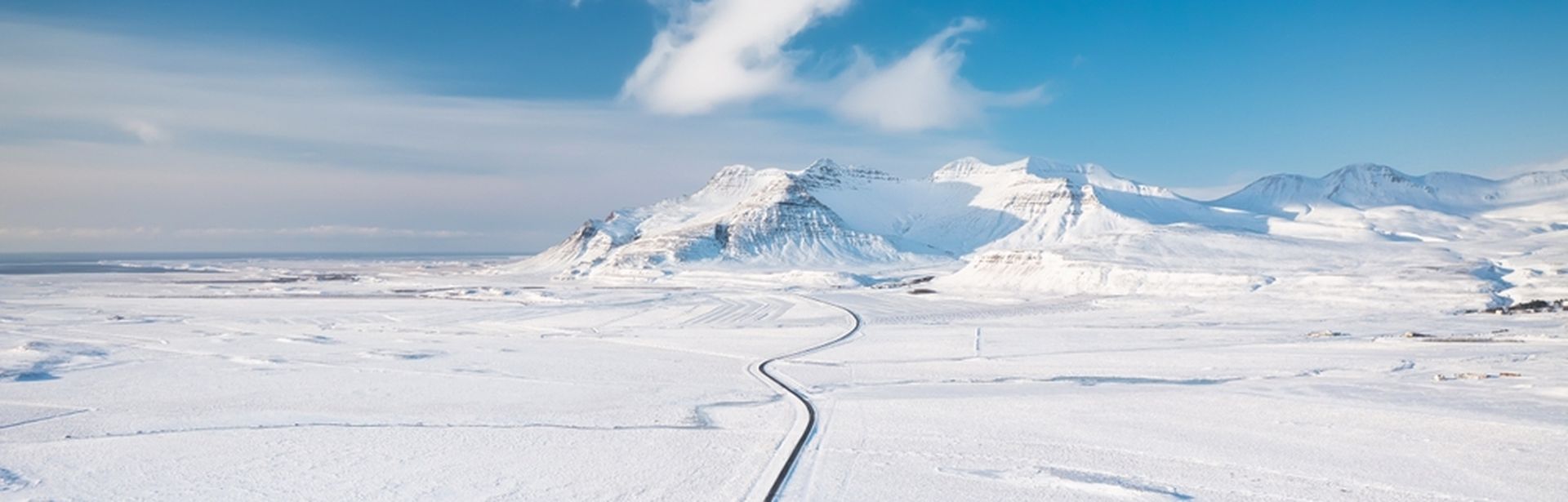 Weg durch eine flache Schneelandschaft mit Bergen im Hintergrund