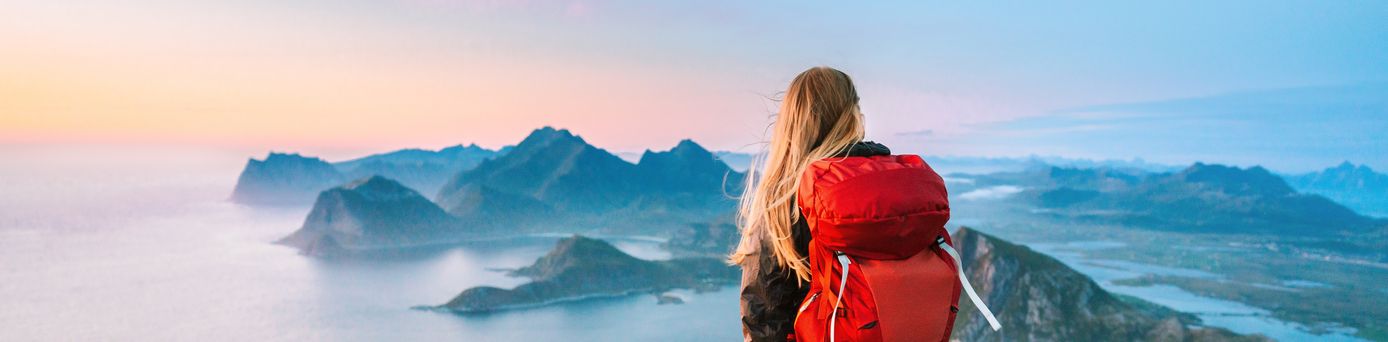 Eine Frau von hinten, Sie trägt einen großen Rucksack und schaut von einem Berg aus den Sonnenaufgang an