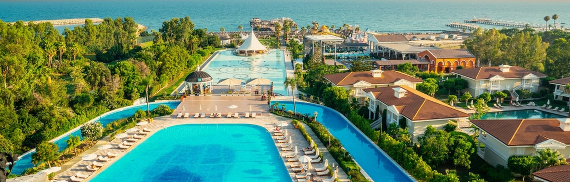 Zwei große Pools umgeben von Bäumen und mit Blick auf das Meer