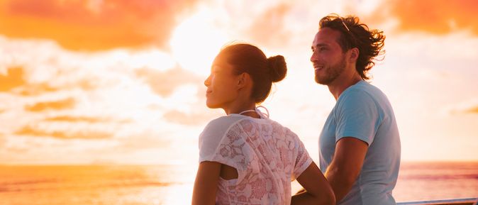 Eine Frau und ein Mann stehen bei Sonnenuntergang an der Reling eines Kreuzfahrtschiffes