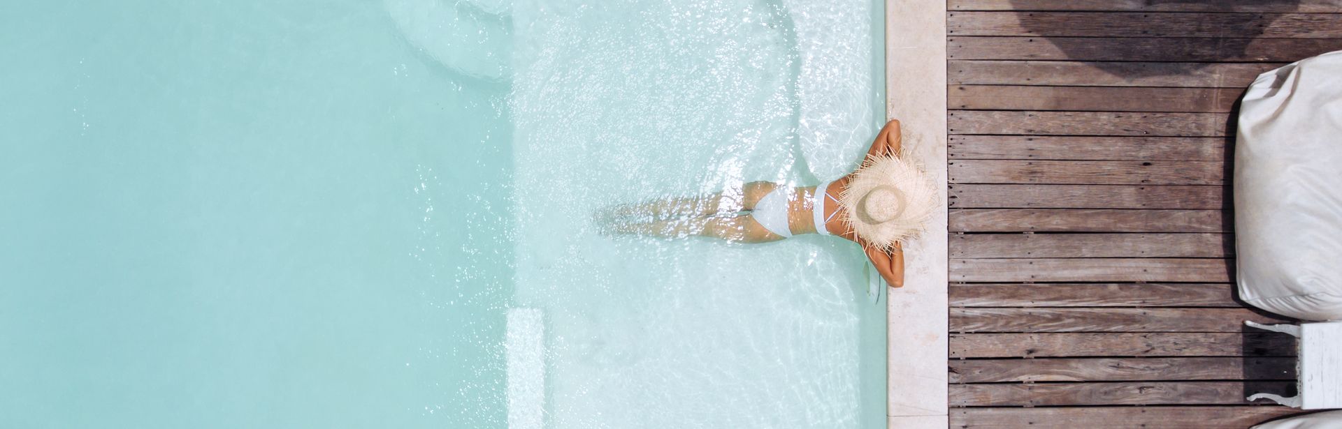 Eine Frau mit weißem Sonnenhut lehnt am Rand eines eleganten Pools