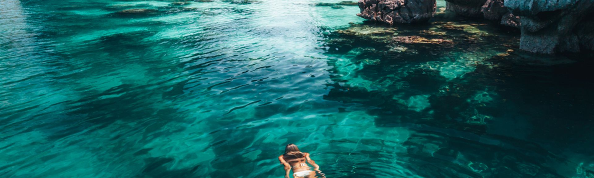 Frau schwimmt im Meer umgeben von Felsen