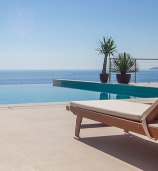 Eine Liege und an einem Infinity Pool, im Hintergrund das Meer