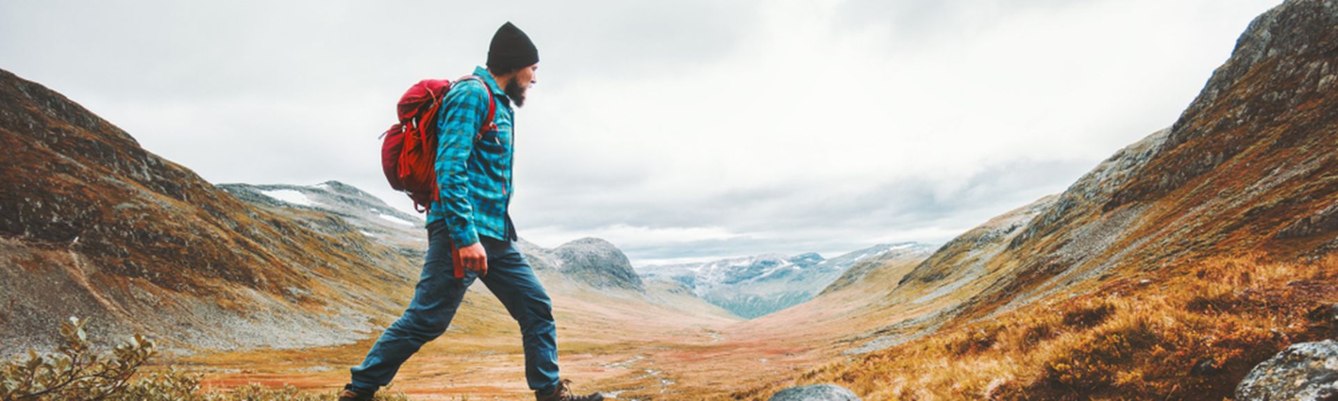 Ein Mann in Wanderkleidung läuft in einer Berglandschaft über Steine in einem Bach