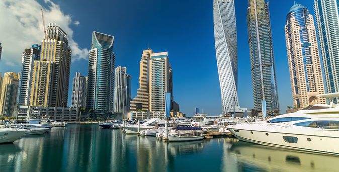 Hochhäuser ragen im Hintergrund empor. Im Vordergrund ist ein kleiner Hafen mit Yachten und kleineren Booten zu sehen