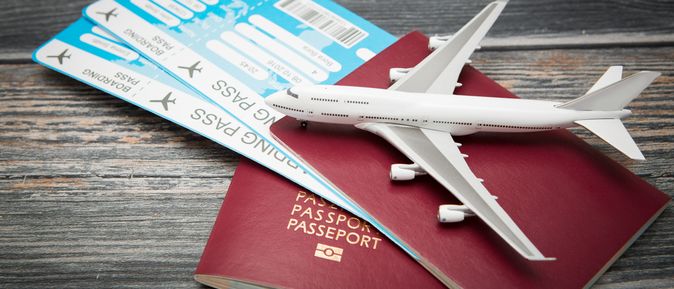 Zwei rote Reisepässe und zwei Flugtickets liegen auf einem Holztisch. Darauf liegt ein Miniaturflugzeug