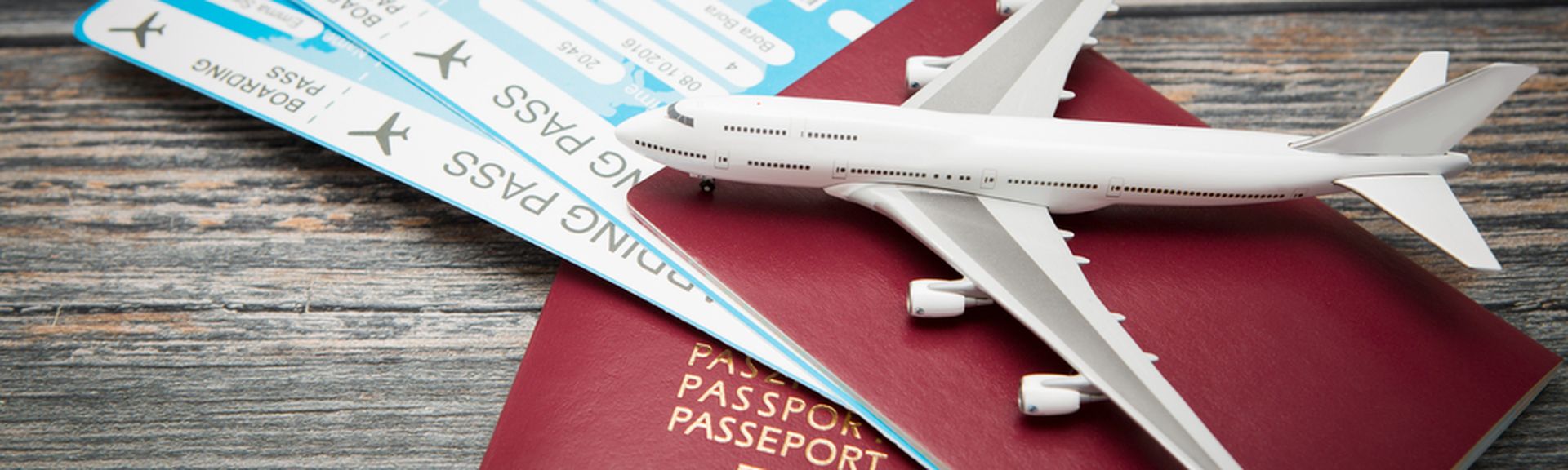 Zwei rote Reisepässe und zwei Flugtickets liegen auf einem Holztisch. Darauf liegt ein Miniaturflugzeug