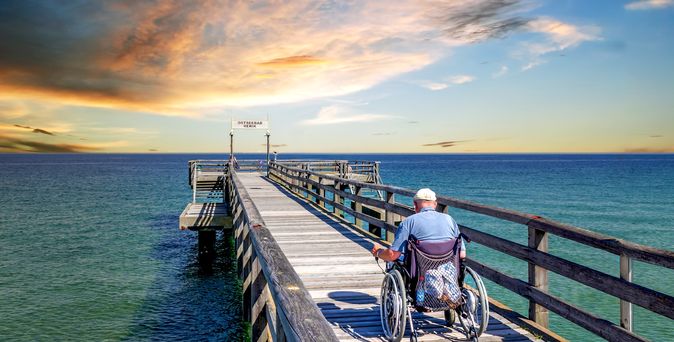 Mann im Rollstuhl auf einer Seebrücke am Meer