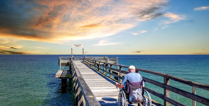 Mann im Rollstuhl auf einer Seebrücke am Meer