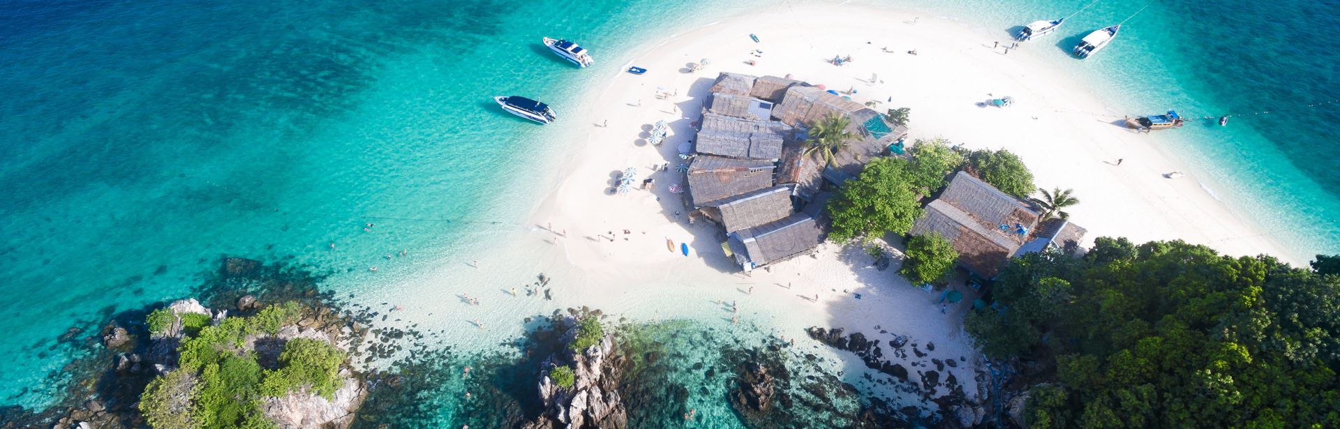Luftaufnahme einer Insel mit Booten im türkisfarbenen Wasser 