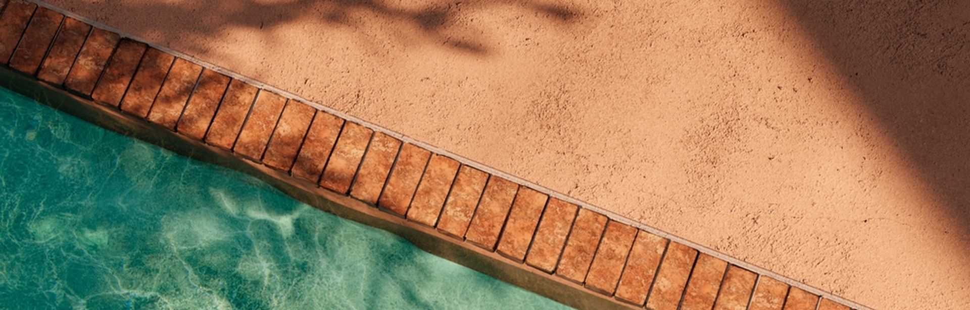 Aus der Vogelperspektive fotografierter Poolausschnitt: Der Rand eines Pools ist links im Bild sichtbar, daneben ein heller Steinboden.