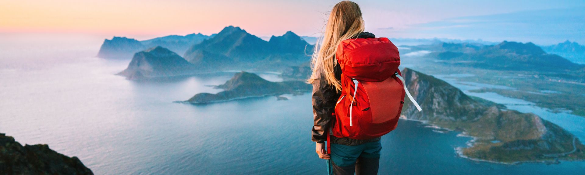 Alleinreisende Frau mit Rucksack schaut von einem Berg auf Wasser 