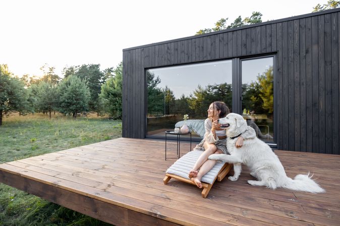 Eine Frau sitzt mit Ihrem Hund auf der Terrasse von einem Ferienhaus