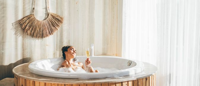 Eine Frau sitzt in einem Whirlpool in einem modernen Hotelzimmer und trinkt ein Glas Sekt