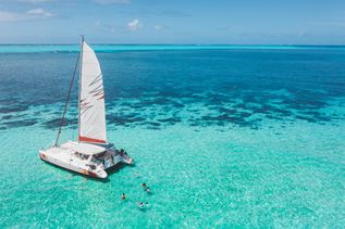 Ein Segelboot im Meer, dahinter schwimmen mehrere Personen
