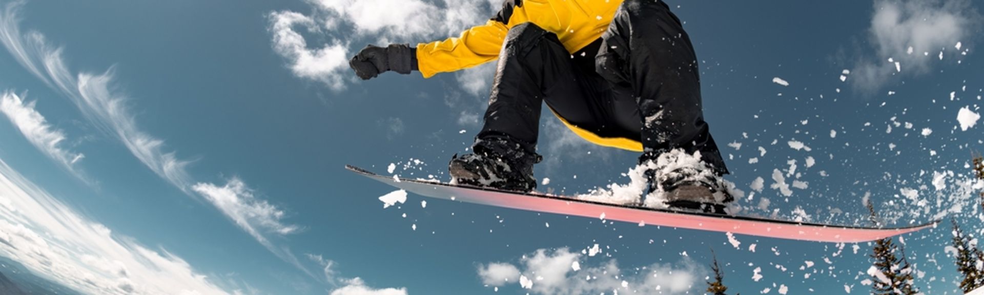 Eine Person in gelber Winterjacke springt mit einem Snowboard durch die Luft