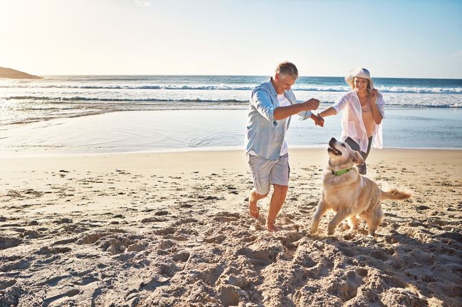 Eine Frau und ein Mann spielen am Strand mit einem Hund 