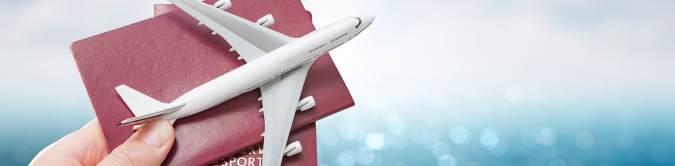 Eine Hand hält vor einem blauen Hintergrund zwei Reisepässe und ein Miniaturflugzeug hoch