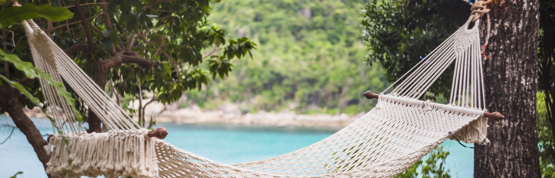 Hängematte zwischen zwei Bäumen, im Hintergund sieht man das Meer
