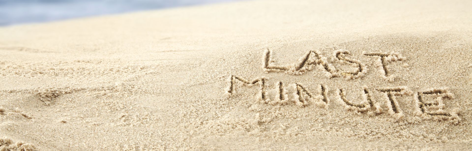 Ein Sonnenuntergang am Strand, im Sand steht "Last Minute" geschrieben