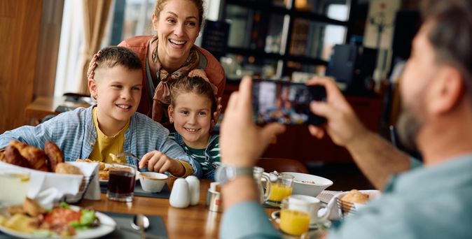 Zwei Kinder und eine Frau werden von einem Mann am Frühstückstisch fotografiert