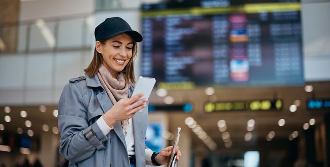 Frau am Flughafen schaut lächelnd auf ihr Smartphone