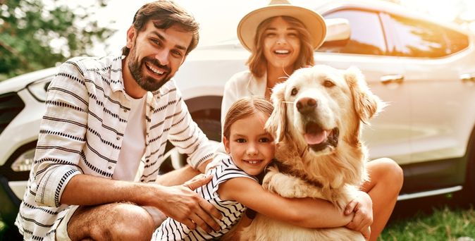 Eine Familie mit einem Kind und einem Hund kniet lächelnd vor einem Auto