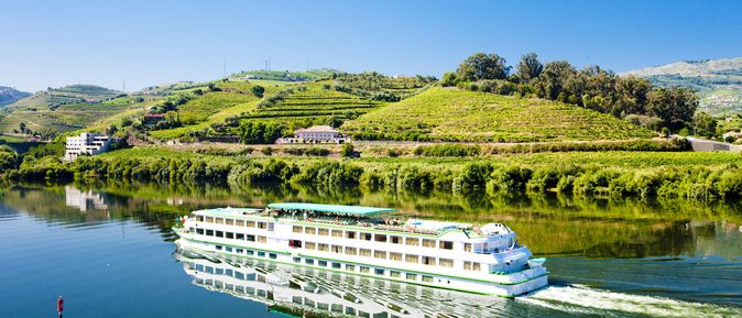 Flusskreuzfahrtschiff, dass durch eine hüglige, grüne Landschaft fährt